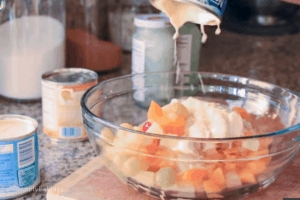 adding the cream to the strained fruit cocktail for filipino fruit salad recipe