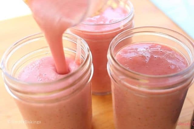 pouring the strawberry banana smoothie into small mason jars