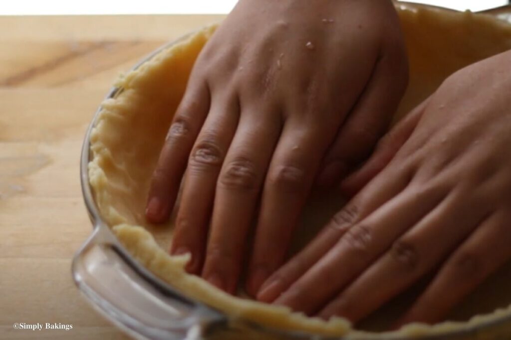 Two hands pressing the dough flat on the surface