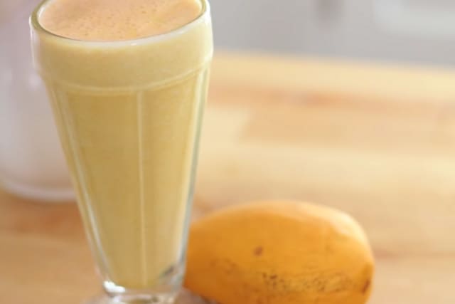 Mango shake in a tall glass and a filipino mango beside it