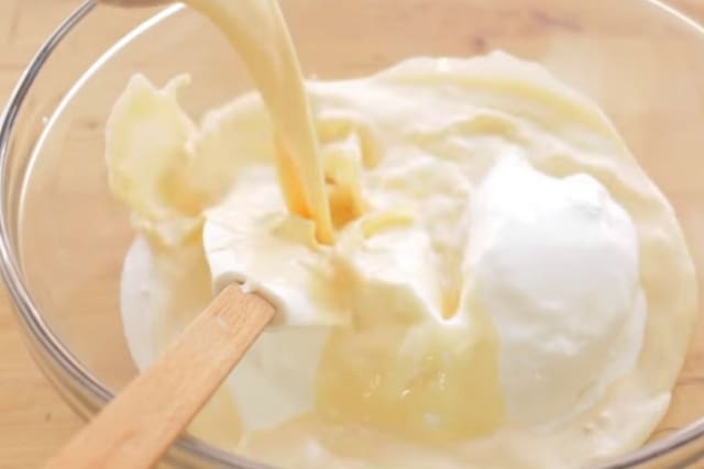pouring evaporated milk over whipped topping on a clear mixing bowl and rubber spatula for 3 ingredient nutella popsicle recipe