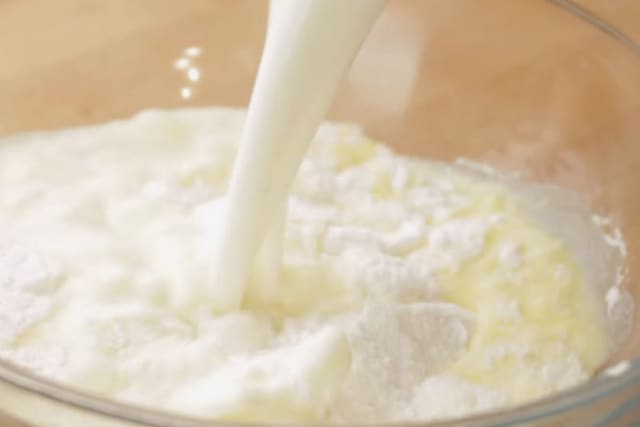 pouring milk to easy lemon cake ingredients on a clear bowl