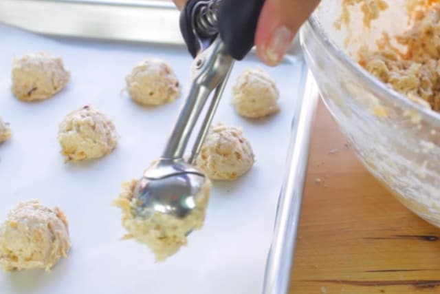 scooping snickerdoodle apple cookie dough onto a baking sheet using an ice cream scoop 