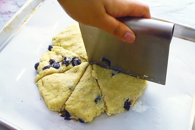 slicing the round blueberry scone dough with a pastry cutter