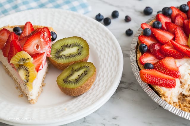 a slice of gluten free and dairy free fruit cheesecake on a white plate with two kiwi slices