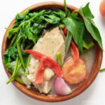 a bowl of vegan sinigang with vegetarian salmon, leafy vegetable, tomato and red bell pepper slices