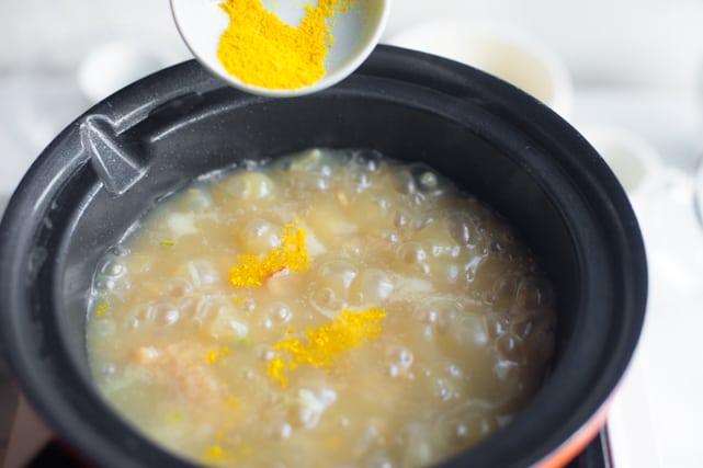 adding turmeric powder to the simmering vegetarian congee