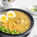 vegetarian congee in a balck bowl topped with boiled egg, green onions and toasted garlic