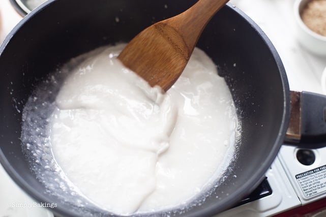heating the coconut milk in a pan and stirring it with a wooden ladle