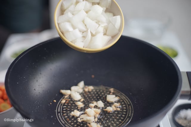 adding onion to the sauteed garlic in the pan for vegan chicken afritada recipe