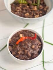 vegan dinuguan in two white bowls with a chili peppers on top