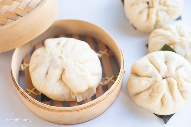 a vegan siopao in a bamboo steamer and three other vegan siopaos with a square-shaped banana leaves at the bottom