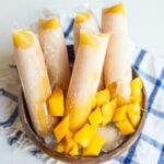 some mango ice candies in a wooden bowl with mango slices and ice cubes
