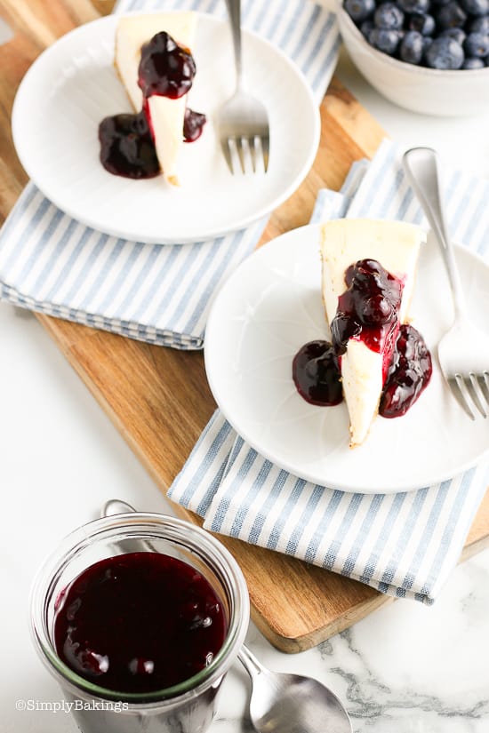 two servings of sliced cheesecakes drizzled with blueberry sauce on a white plate with a fork