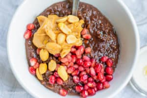 a bowl of chocolate oatmeal with a stainless steel serving spoon and topped with pomegranate seeds, peanut butter and peanuts