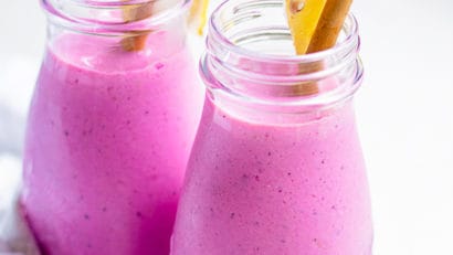 two glasses of dragon fruit smoothies with a straw on each glass and garnished with a sliced lemon