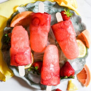 Grapefruit Strawberry Popsicles on a round plate with ice and fresh strawberries