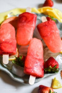 Grapefruit Strawberry Popsicles with ice and fresh strawberries on a round plate