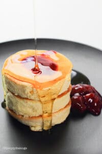 fluffy Japanese panckes on a black plate with sweet berry sauce