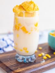 a tall glass of mais con yelo on a wooden board and garnished with corn kernels