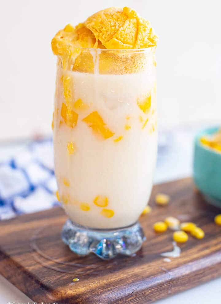 a tall glass of mais con yelo on a wooden board and garnished with corn kernels