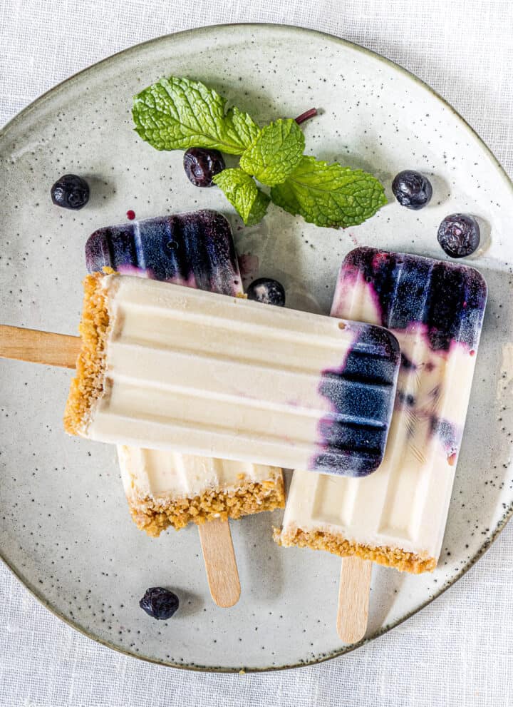 blueberry popsicles on a white plate and garnished with mint leaves and blueberries