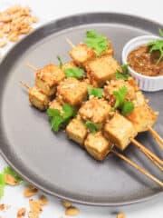 tofu skewers on a peanut sauce of a gray plate