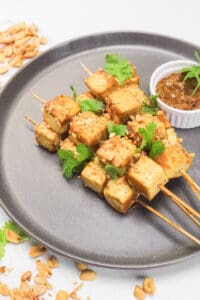 tofu skewers on a peanut sauce of a gray plate