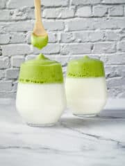 two cups of dalgona matcha with a wooden spoon