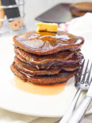 a stack of ube pancakes on a white plate with a stainless fork on the side