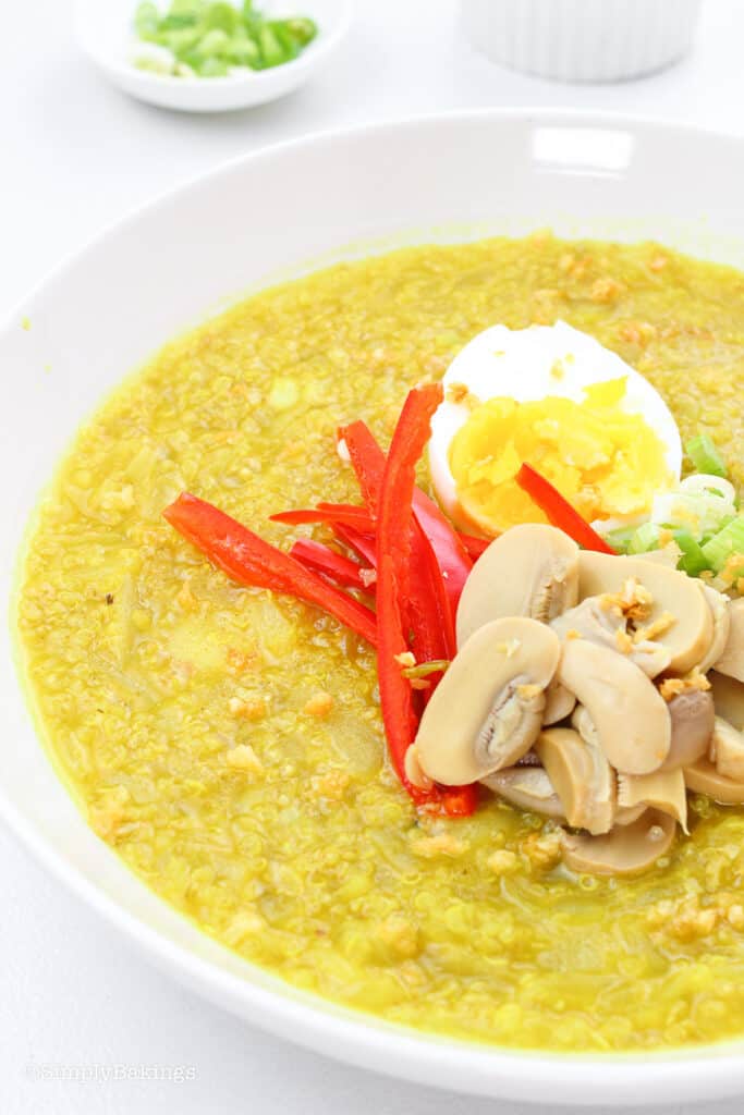 a bowl of arroz caldo topped with mushroom slices, hard-boiled egg, chopped green onions and sliced bell pepper