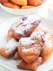 ube beignets with confectioner's sugar served on a white plate and bowl