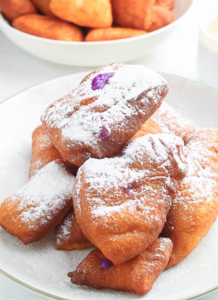 ube beignets with confectioner's sugar served on a white plate and bowl