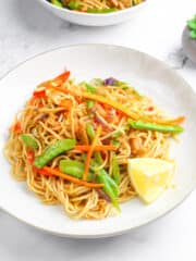 vegan pancit canton on a white plate with a slice of lemon on the side