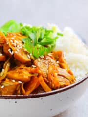 delicious savory vegan jackfruit dish garnished with sesame seeds and green onions on white rice in a bowl