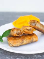 4 lumpia on a white plate garnished with mango and an herb