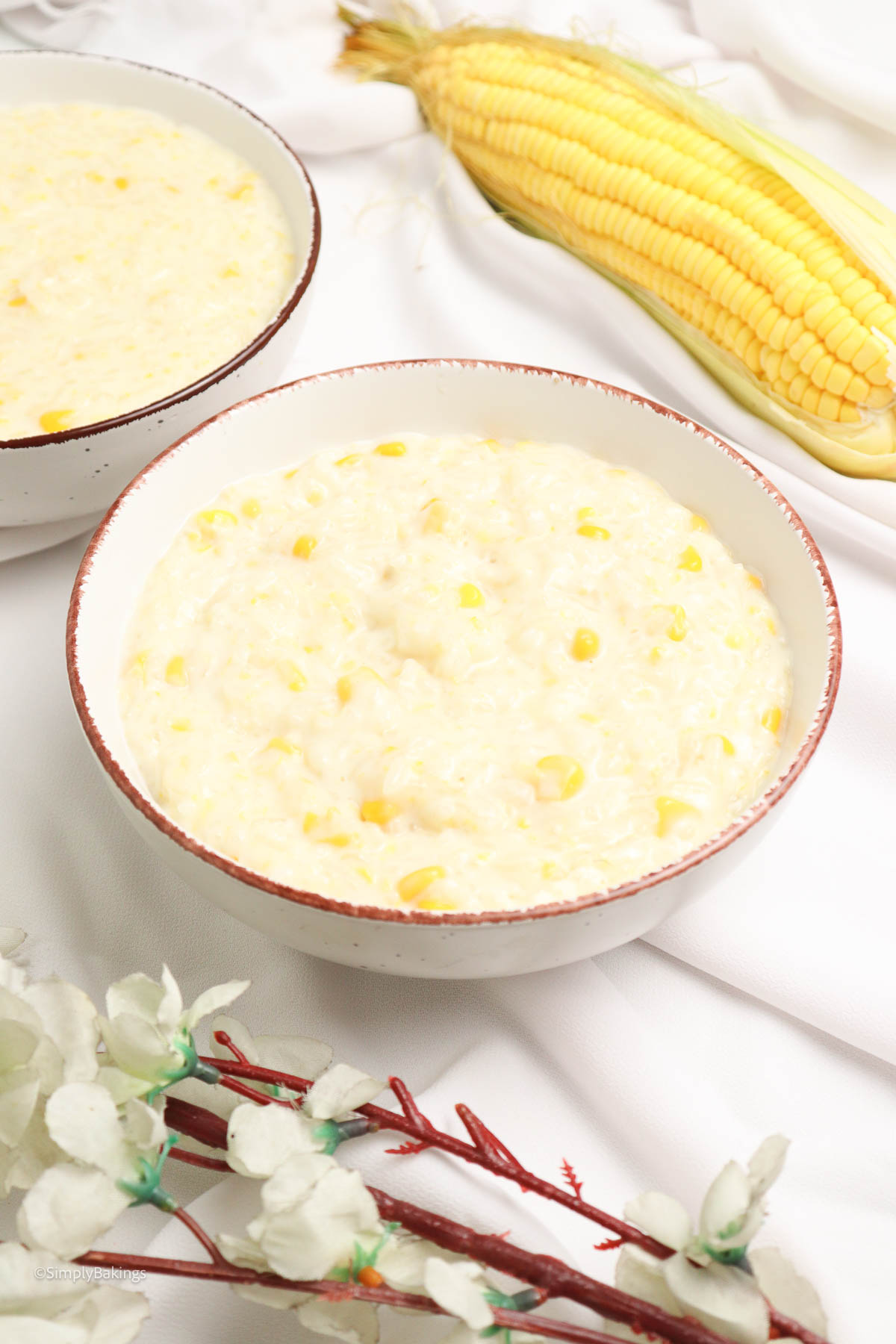 delicious Filipino ginataang mais served in bowls beside a fresh sweet corn and a few white flowers