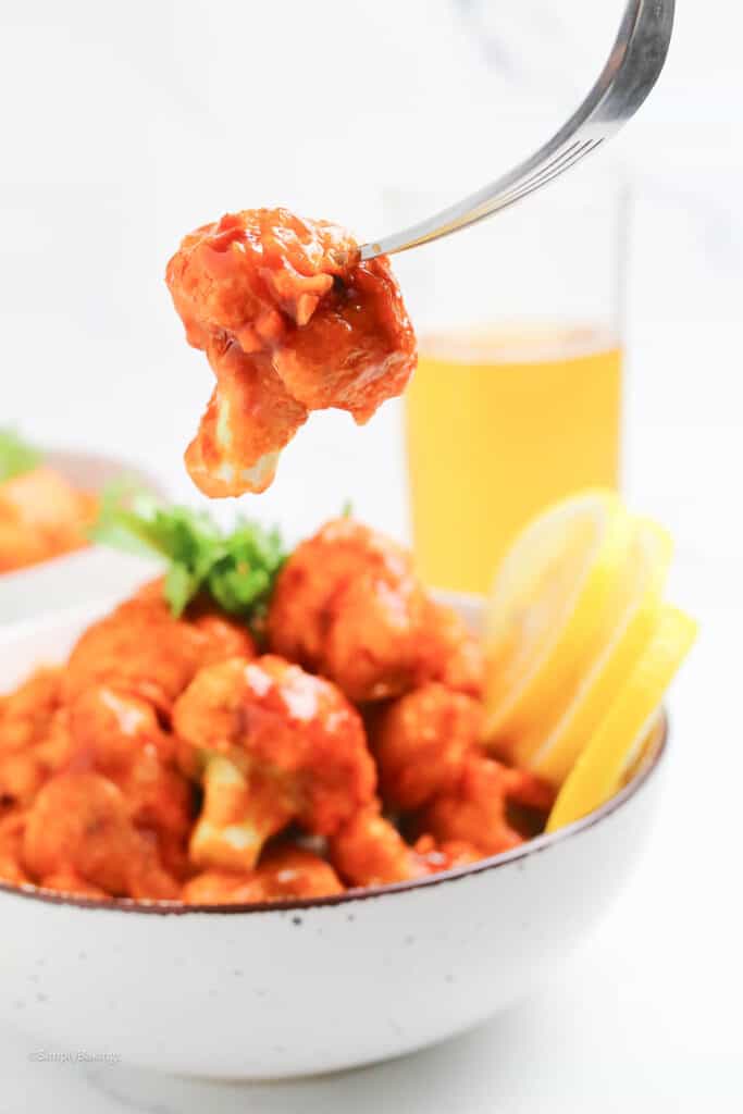 a forkful of saucy cauliflower bites with huli huli sauce served with juice, image created by SimplyBakings