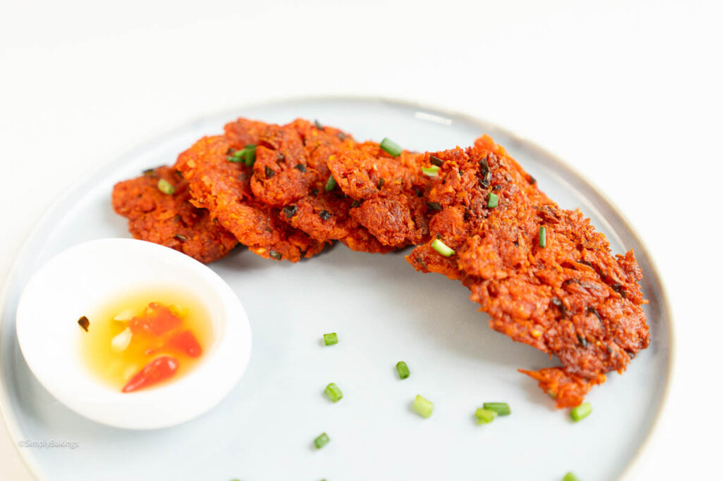 some fried okoy and a dipping sauce served on a white plate garnished with chopped spring onions