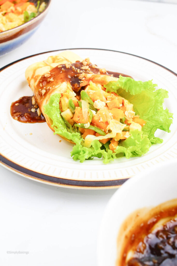 lumpiang sariwa served on a white plate drizzled with peanut sauce