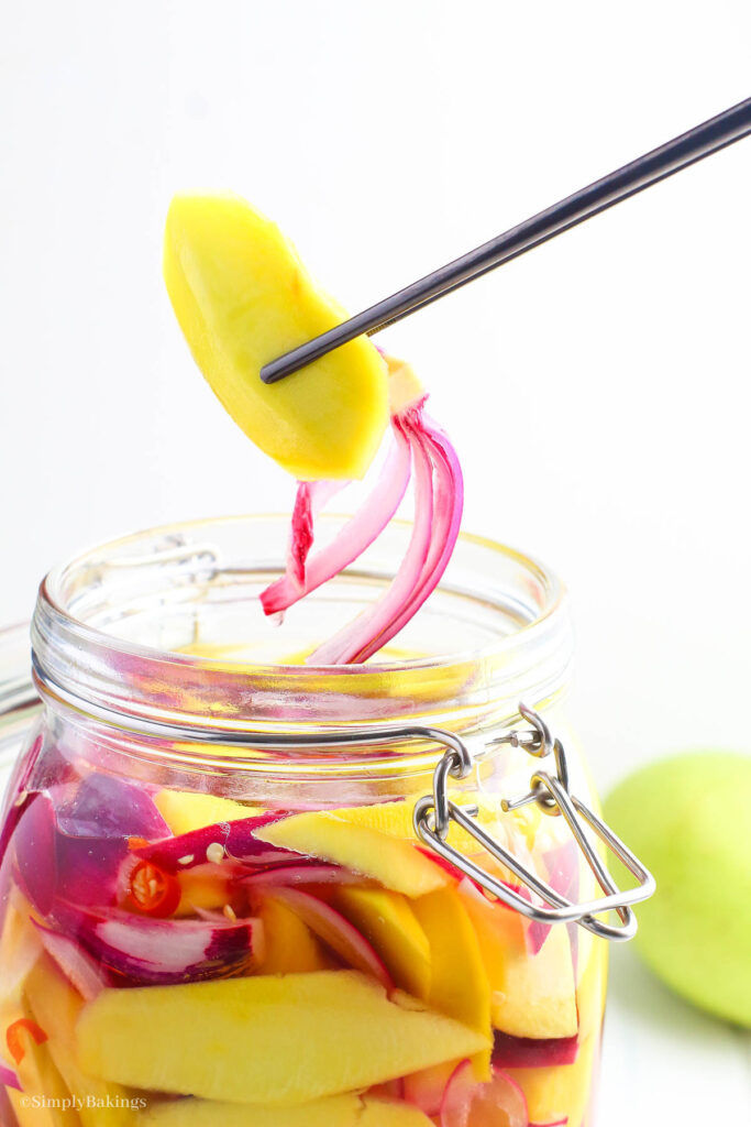 pickled mango and red onion held by black chopsticks over a jar