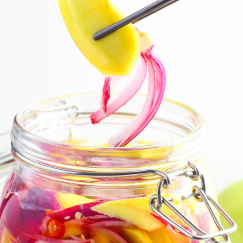a jar of pickled mangoes with red chilies and red onion slices