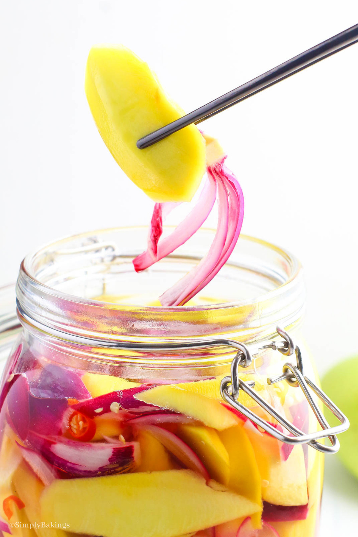 a jar of pickled mangoes with red chilies and red onion slices
