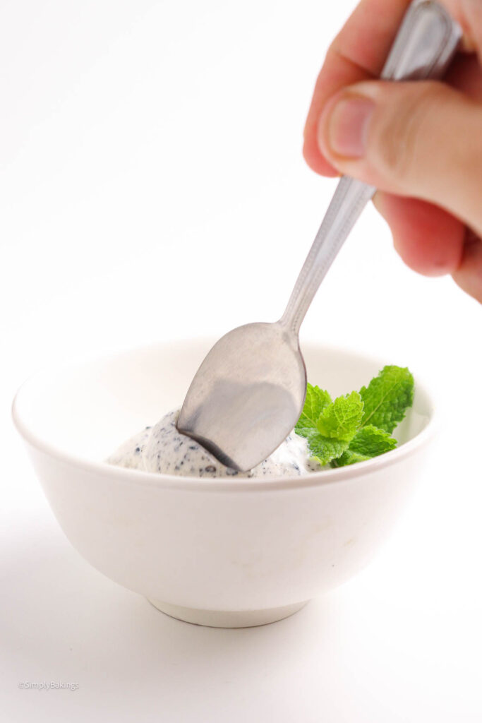 scoops of black Sesame ice cream garnished with mint leaves and spoon held by a hand