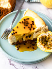 a slice of Passion Fruit Cheesecake on a dessert plate beside a stainless fork and half of passion fruit
