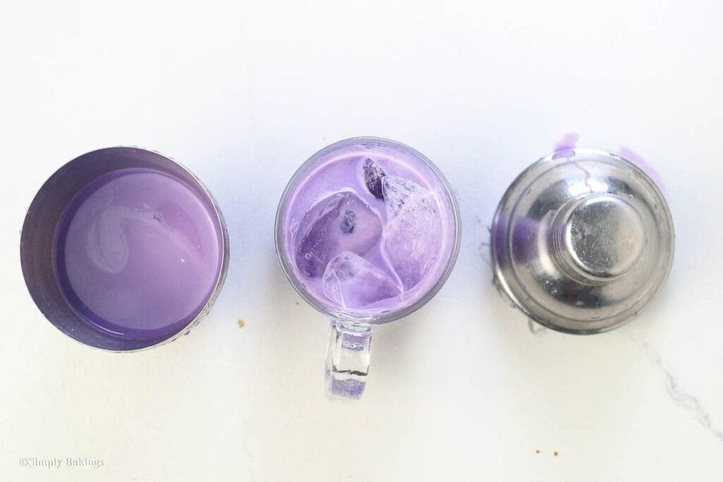 A glass mug with iced ube mixture next to steel cups