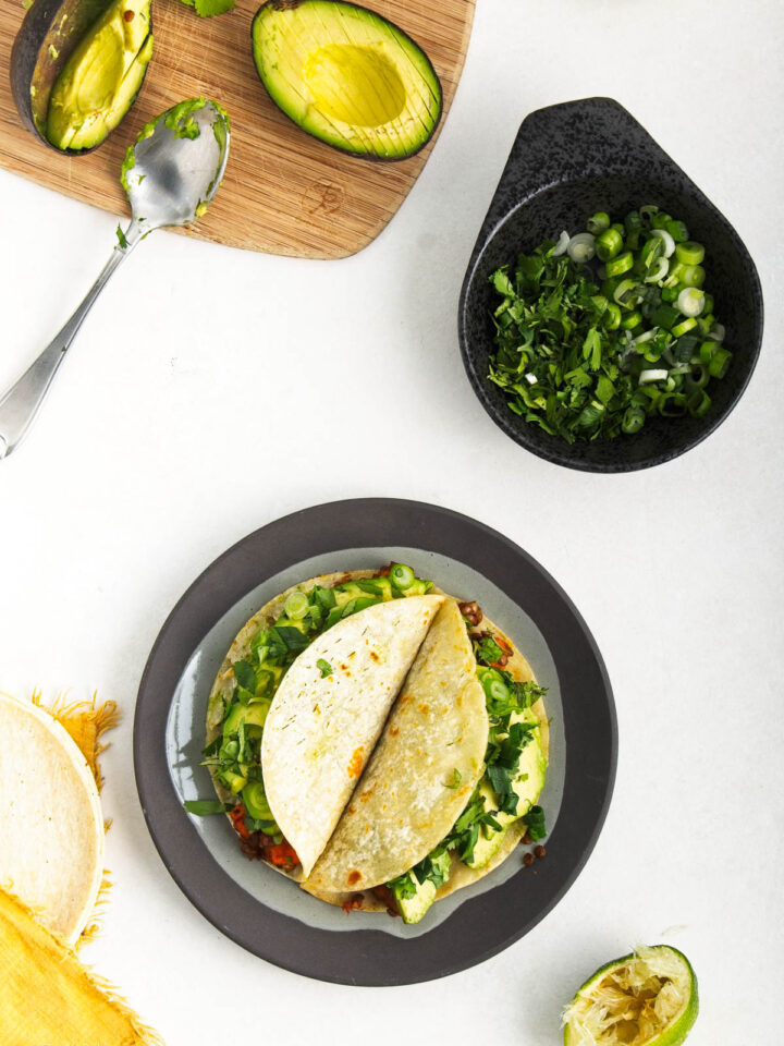 A plate of lentil tacos next to avocadoes