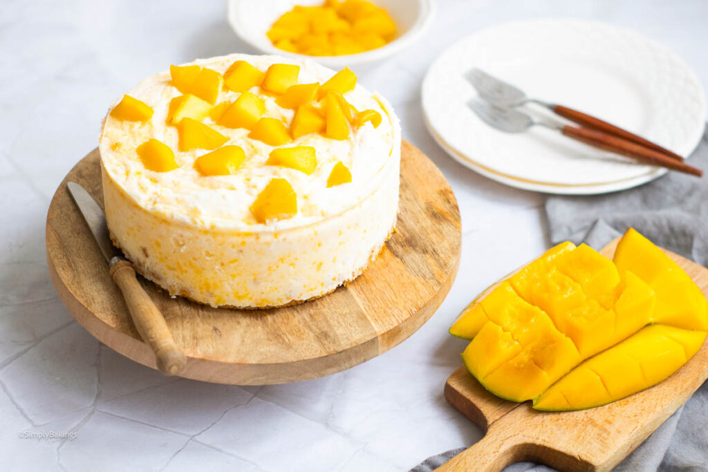 mango cheesecake on a circular wooden board with a knife and a slice of mango on another wooden board