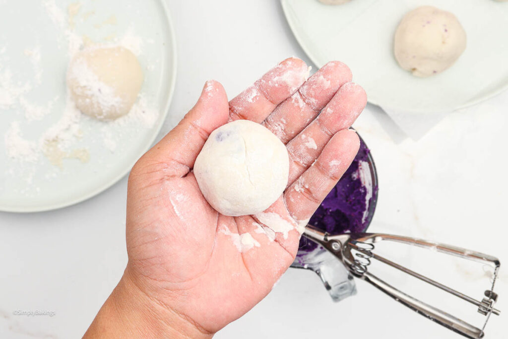 A hand holding up a taro bun dough ball