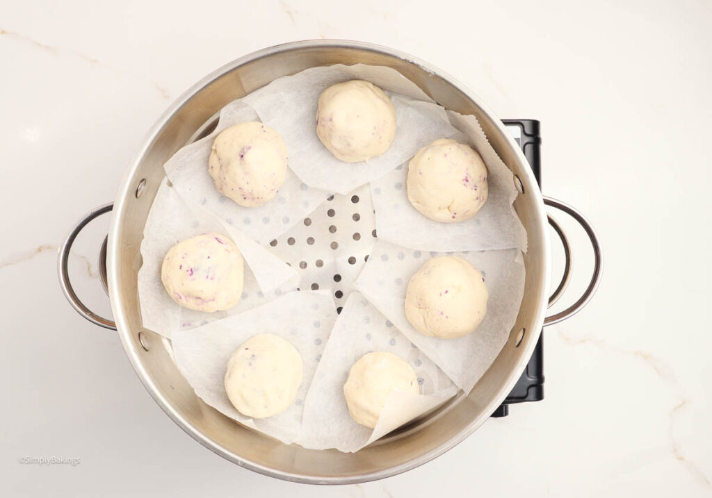 Taro buns with parchment papers arranged neatly in a steamer